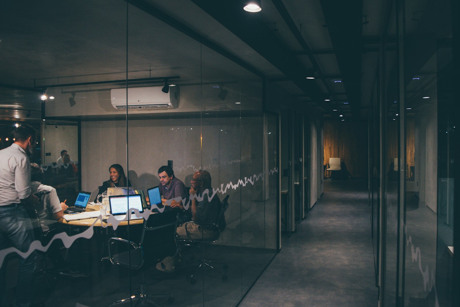 Team collaborating around laptops in a glass-walled meeting room